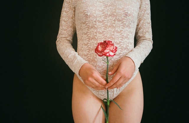 Žena v čipkovanom body drží pred svojim bruchom červenú ružu
