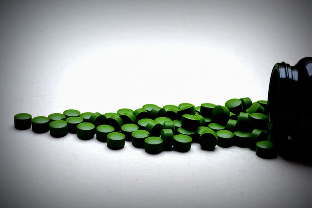 Zelené tabletky vysypané z fľaštičky na bielom stole.jpg