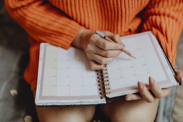 Žena v oranžovom svetri sedí na kresle a píše do diára s kalendárom.jpg